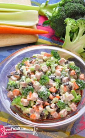 Brócoli picado, mezclado con verduras, nueces picadas y aderezo, se muestra en un tazón para servir.