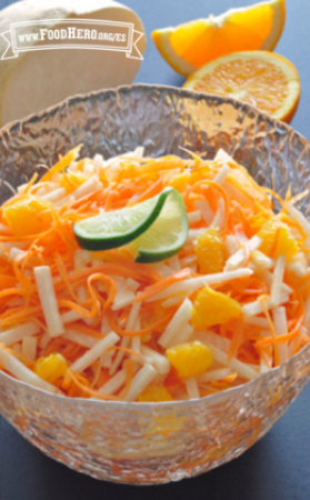 Rodajas crujientes de jícama y zanahoria con naranjas adornadas con limón verde en un recipiente de vidrio.