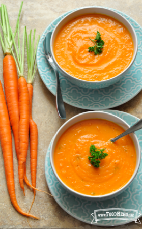 Bowls of smooth carrot soup on serving plates.