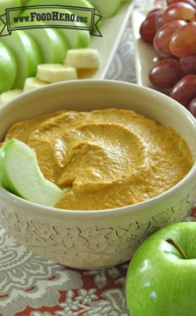 Small bowl of pumpkin dip served with apple slices, banana and grapes.