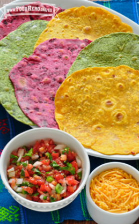 Tortillas de colores brillantes servidas junto con queso rallado y salsa.