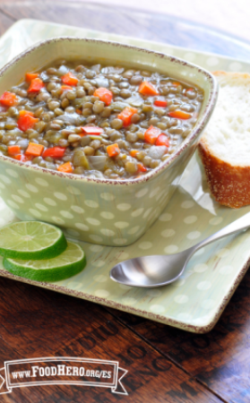 Sopa de lentejas, zanahorias y pimientos dulces servida con limón verde y una rebanada de pan.