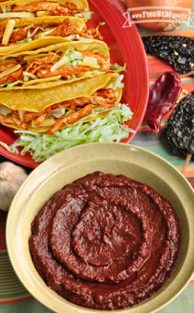 Tazón mediano de salsa espesa de adobo rojo, servida con tacos.
