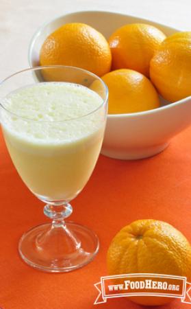 Footed glass filled with a frothy orange juice drink.
