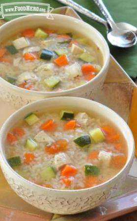 Two bowls of soup filled with rice, chicken and vegetables. 