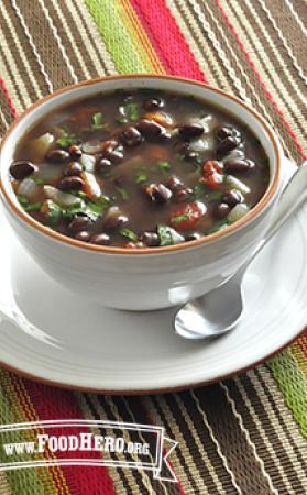 A bowl of warming soup with black beans and vegetables, garnished with herbs.