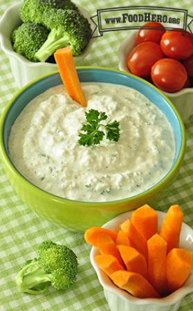 Bowl of creamy dip garnished with parsley and served with raw carrots, cherry tomatoes and broccoli. 