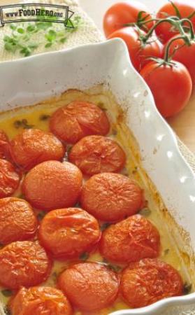 Roasted tomato halves and herbs with a small amount of liquid in the bottom of the baking dish.