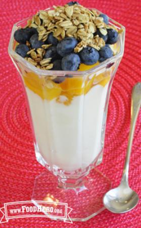 Glass cup with layers of yogurt, peach, blueberries and granola.