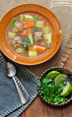 Bowl of meatballs, rice and vegetable soup served with lime and cilantro. 