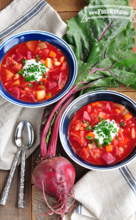 Bowls of vibrant red beet and vegetable soup with a dollop of sour cream and parsley.  