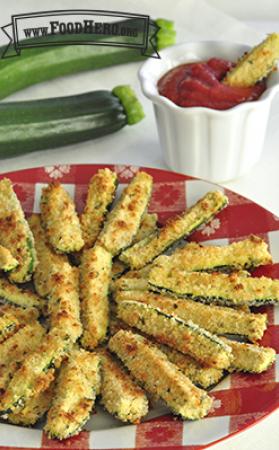 Breaded and baked zucchini slices are shown on a serving platter with a side of marinara sauce.