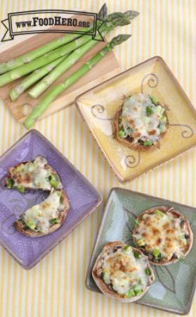 English muffins topped with chopped asparagus, mushrooms and broiled cheese are shown on plates.