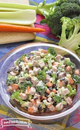 Chopped broccoli, mixed with vegetables, chopped nuts and dressing, is displayed in a serving bowl.