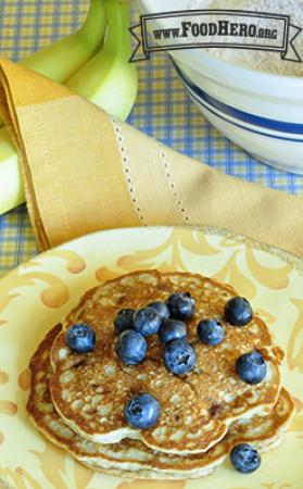 Two golden brown banana pancakes are topped with fresh blueberries.