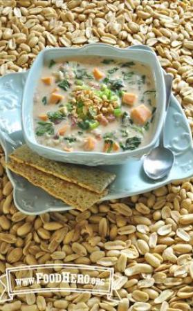 Medium bowl of vegetable and peanut soup on a plate served with crackers.