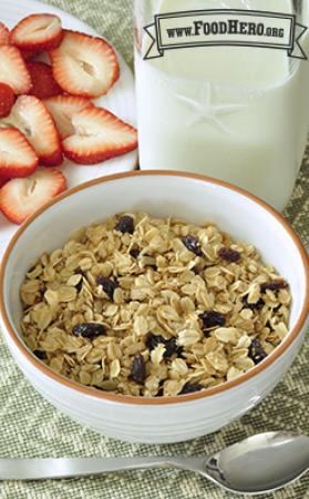 Bowl of rolled oats and raisins served with milk and strawberries.