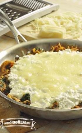 Skillet full of noodles, beef and vegetables under a layer of melted mozzarella cheese. 