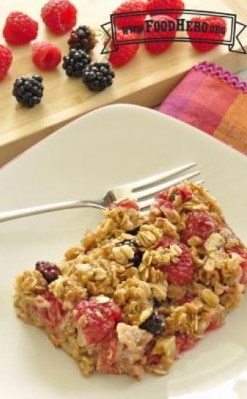 A piece of spiced baked oatmeal with juicy blackberries and raspberries is shown on a plate.