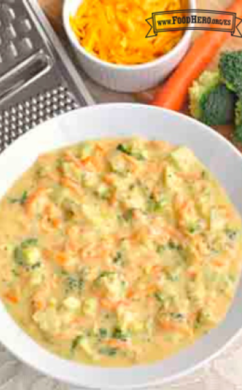 Un tazón de sopa caliente hecha con queso cheddar, zanahorias y brócoli.