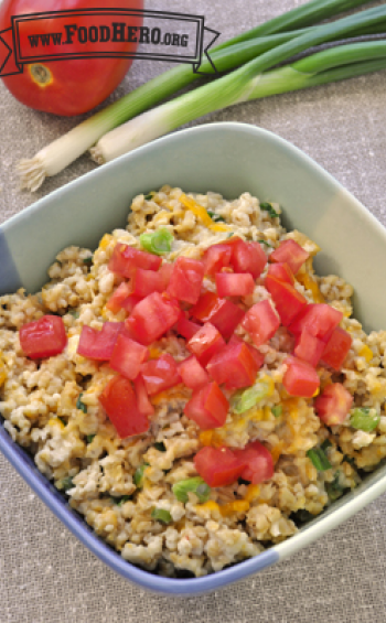 Bowl of cheesy oatmeal topped with chopped tomatoes.