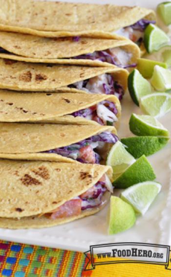 Platter of corn tortillas with creamy slaw and fish filling served with lime wedges.