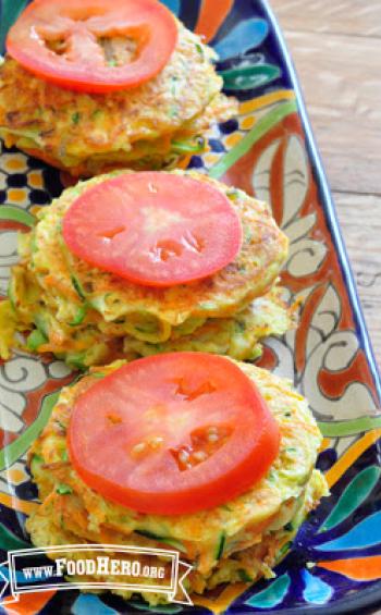 Platter of stacked vegetable patties with a tomato slice. 