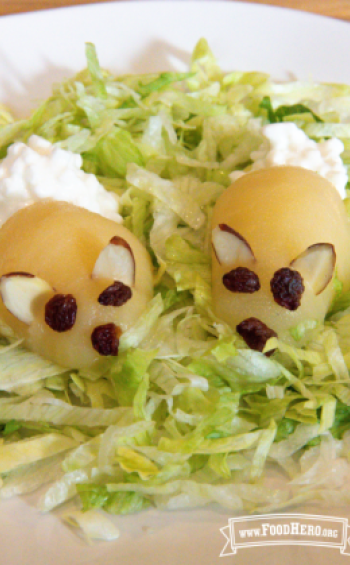 Peeled pear on a lettuce bed with almonds, cottage cheese and raisins appearing like a bunny.