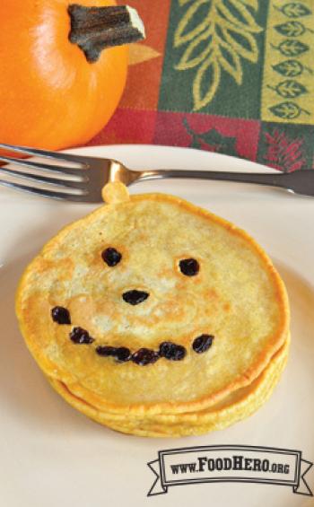 Stack of pumpkin shaped pancakes with raisins.