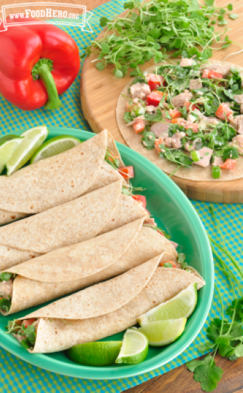 Tortillas folded over a creamy vegetable filled tuna mixture with lime wedges on a plate.