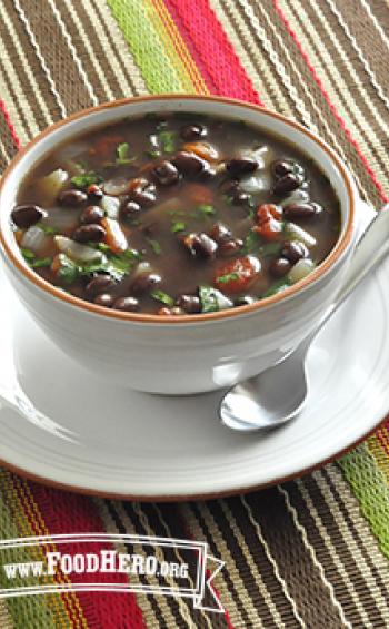 A bowl of warming soup with black beans and vegetables, garnished with herbs.