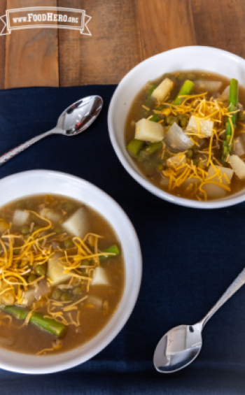 Bowl of soup with asparagus and potatoes topped with cheddar cheese.