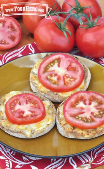 Plate of english muffin halves with cheese and a tomato slice.