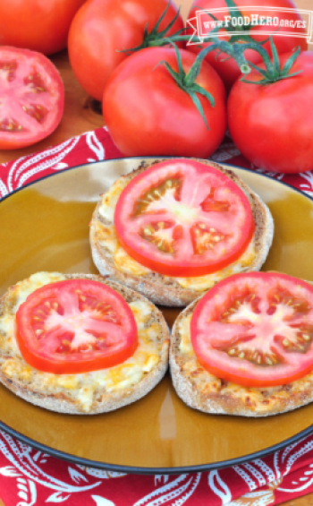 Plato con mitades de panecillos ingleses con queso y una rodaja de tomate.