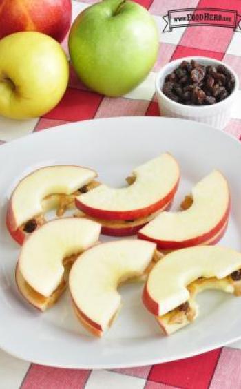 Crispy apple slices with peanut butter and raisin filling are shown on a plate.