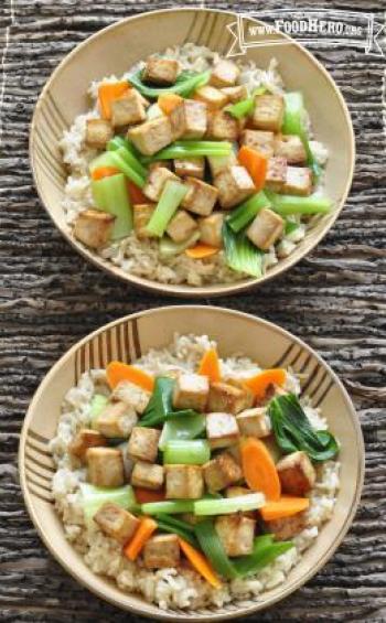 Marinated tofu cubes are baked and combined with stir-fry vegetables and shown over bowls of brown rice.