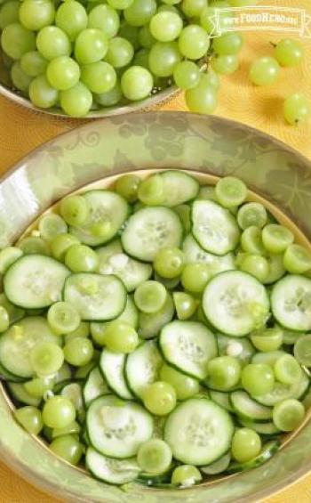 Thinly sliced cucumber and grape halves with dressing in a bowl.