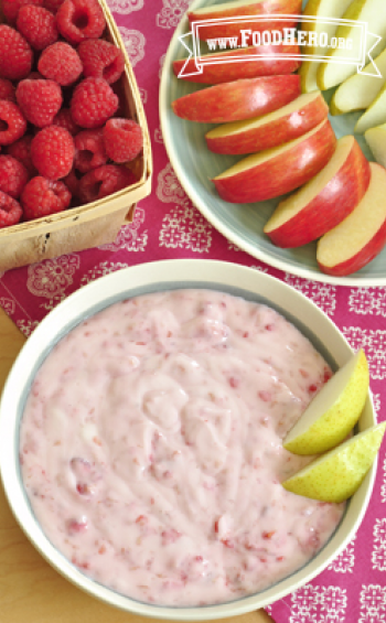 Bowl of yogurt raspberry dip served with sliced apple and pear.